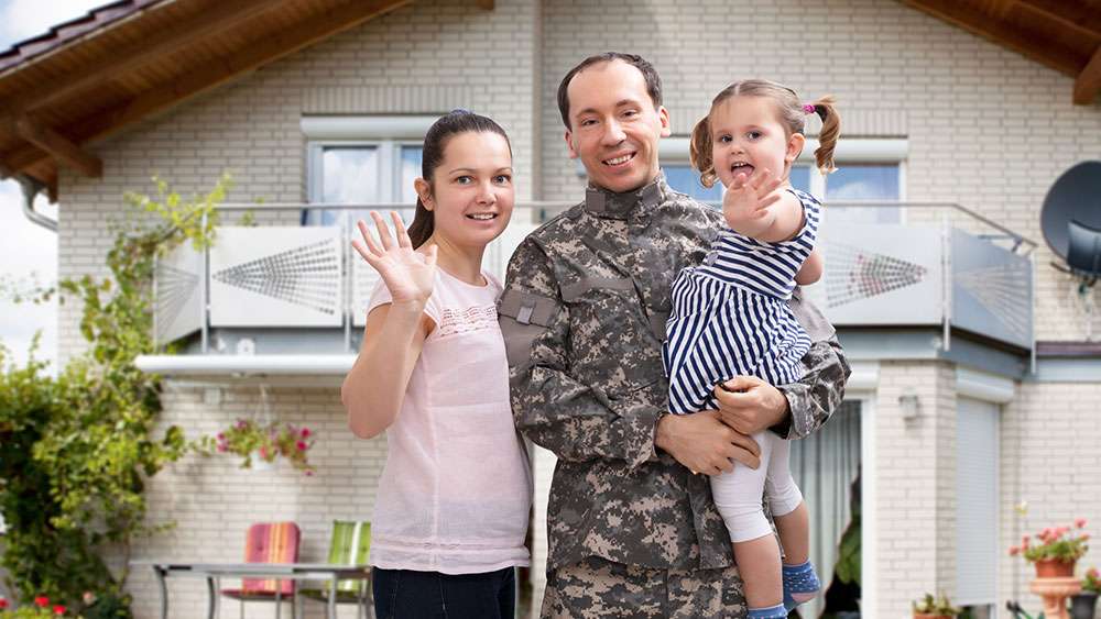 Military man with family standing in front of new home